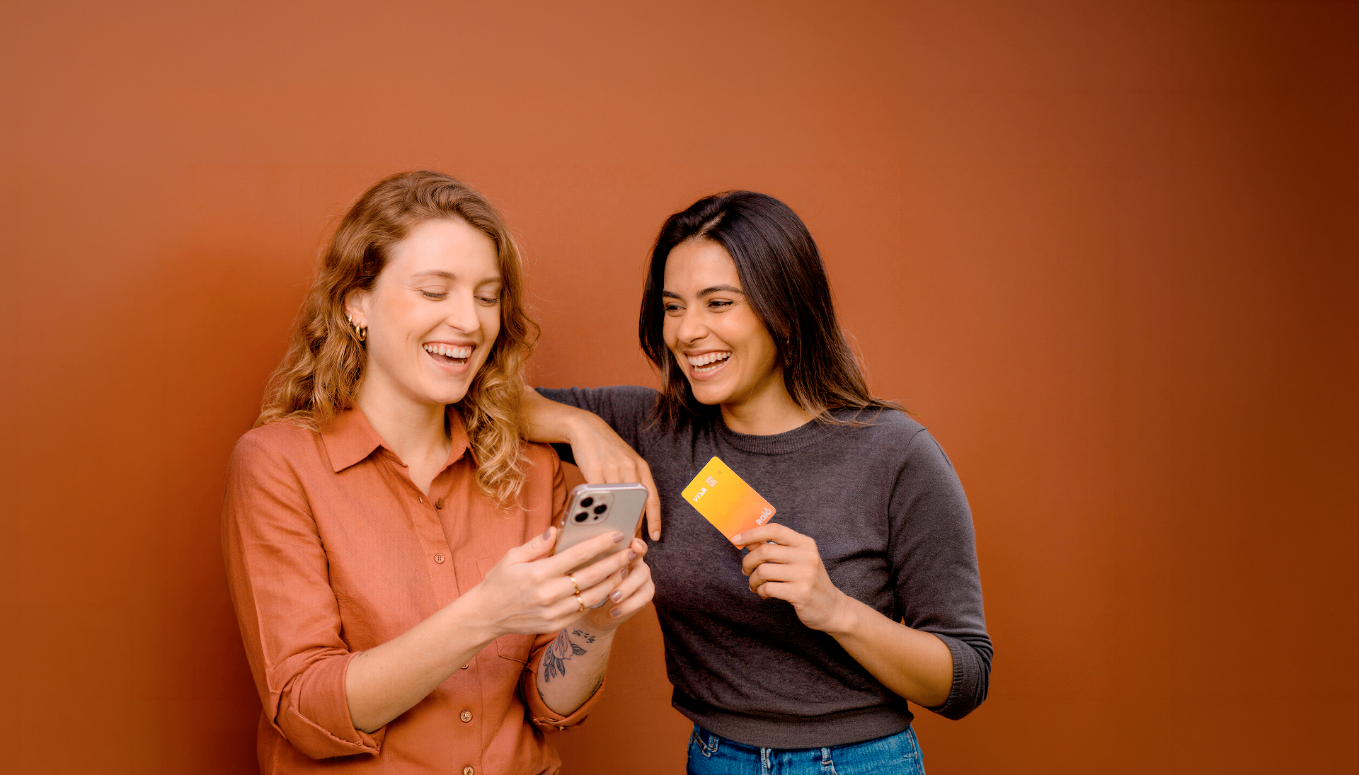 Duas colaboradoras sorrindo com um celular e um cartão Raiô